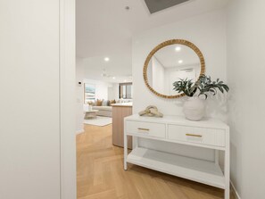 Ein modernes Interieur mit einem weißen Konsolentisch, einem runden Spiegel mit Holzrahmen und einer Topfpflanze.