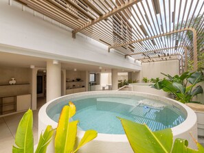Una piscina interior con suelo de baldosas, rodeada de plantas y una estructura de techo de madera.