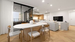 Uma sala de estar moderna com área de jantar, conjunto de sofá, televisão de tela plana e cozinha ao fundo.