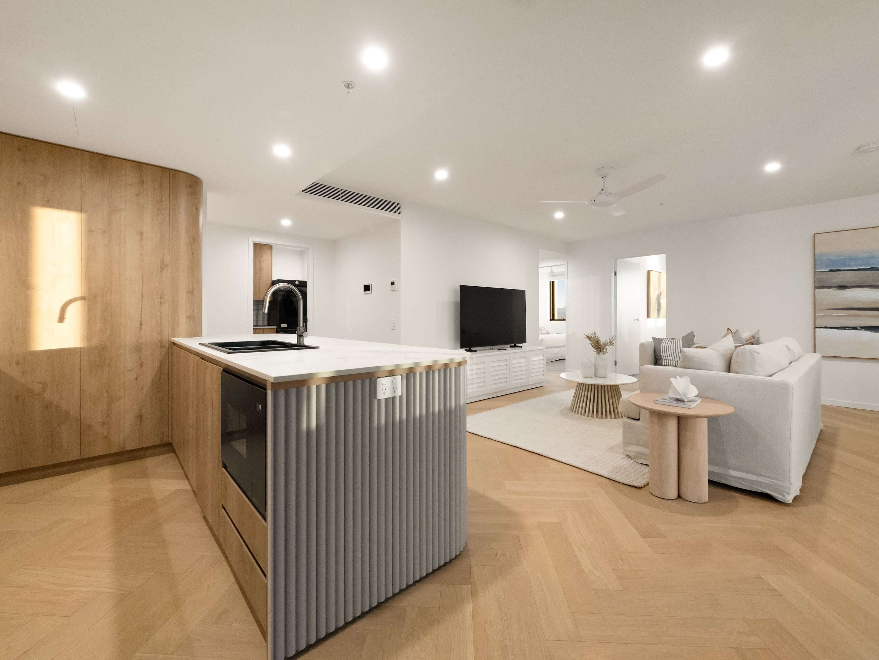 A modern kitchen with a built-in oven, a central island with a sink, and a flat-screen TV.