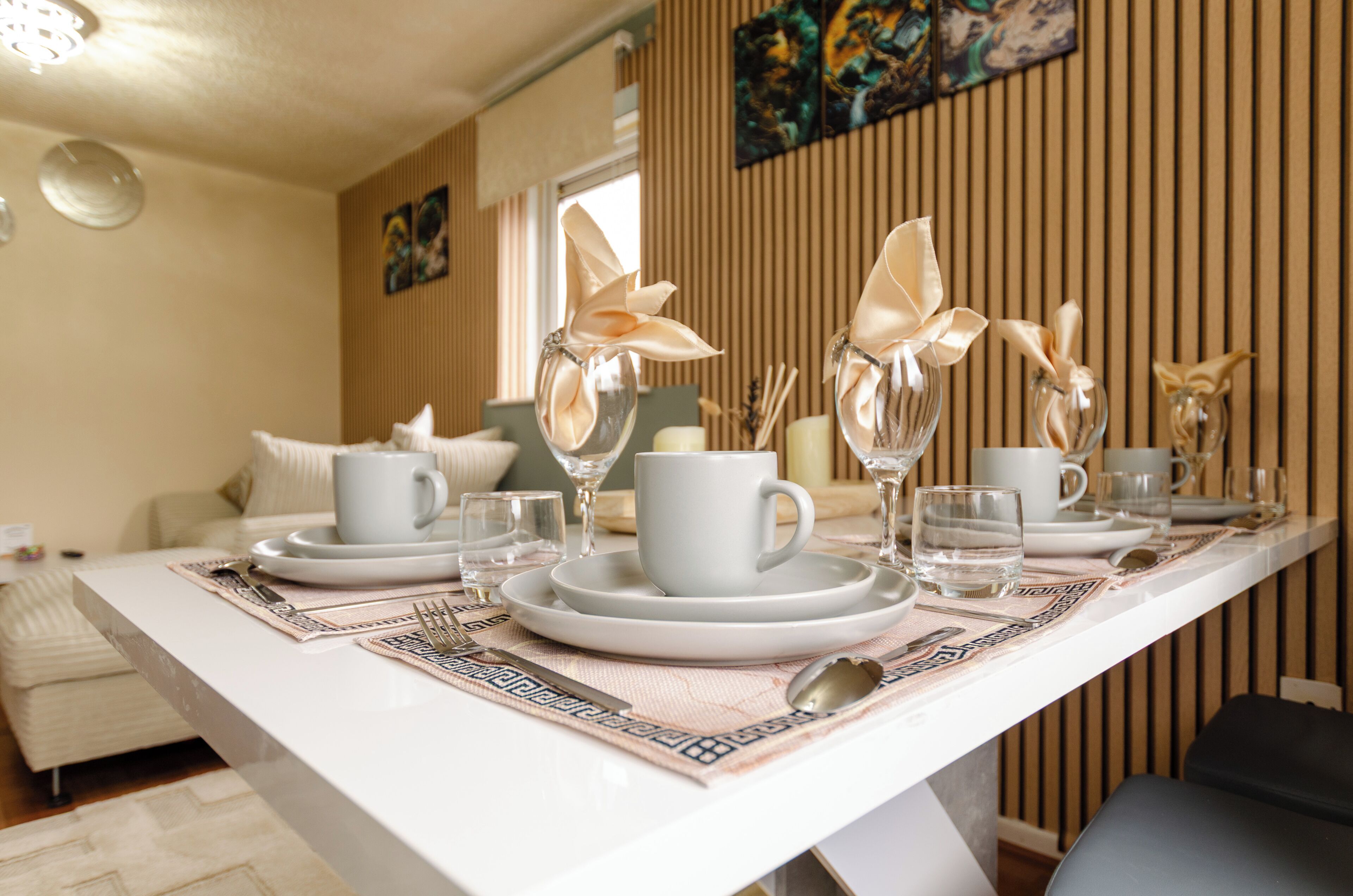 A dining table set with plates, cups, and cutlery, with a modern interior design and artwork on the wall.