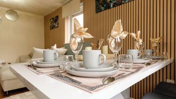 A dining table set with plates, cups, and cutlery, with a modern interior design and artwork on the wall.