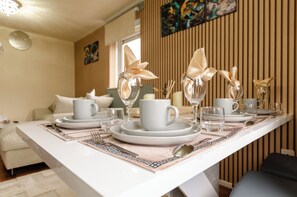 A dining table set with plates, cups, and cutlery, with a modern interior design and artwork on the wall. - Modern Bungalow • Free Parking • Fast WiFi • Near City Centre (Preston)