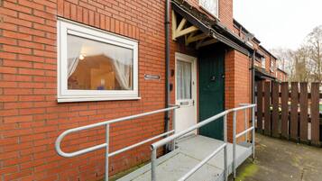 A red brick building with a white door, a 'Welcome' sign, and a ramp leading to the entrance.