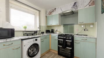 A compact kitchen with a washing machine, microwave, stove, and oven.