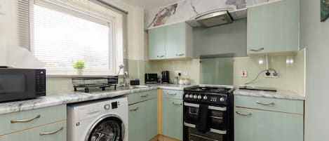 A compact kitchen with a washing machine, microwave, stove, and oven.