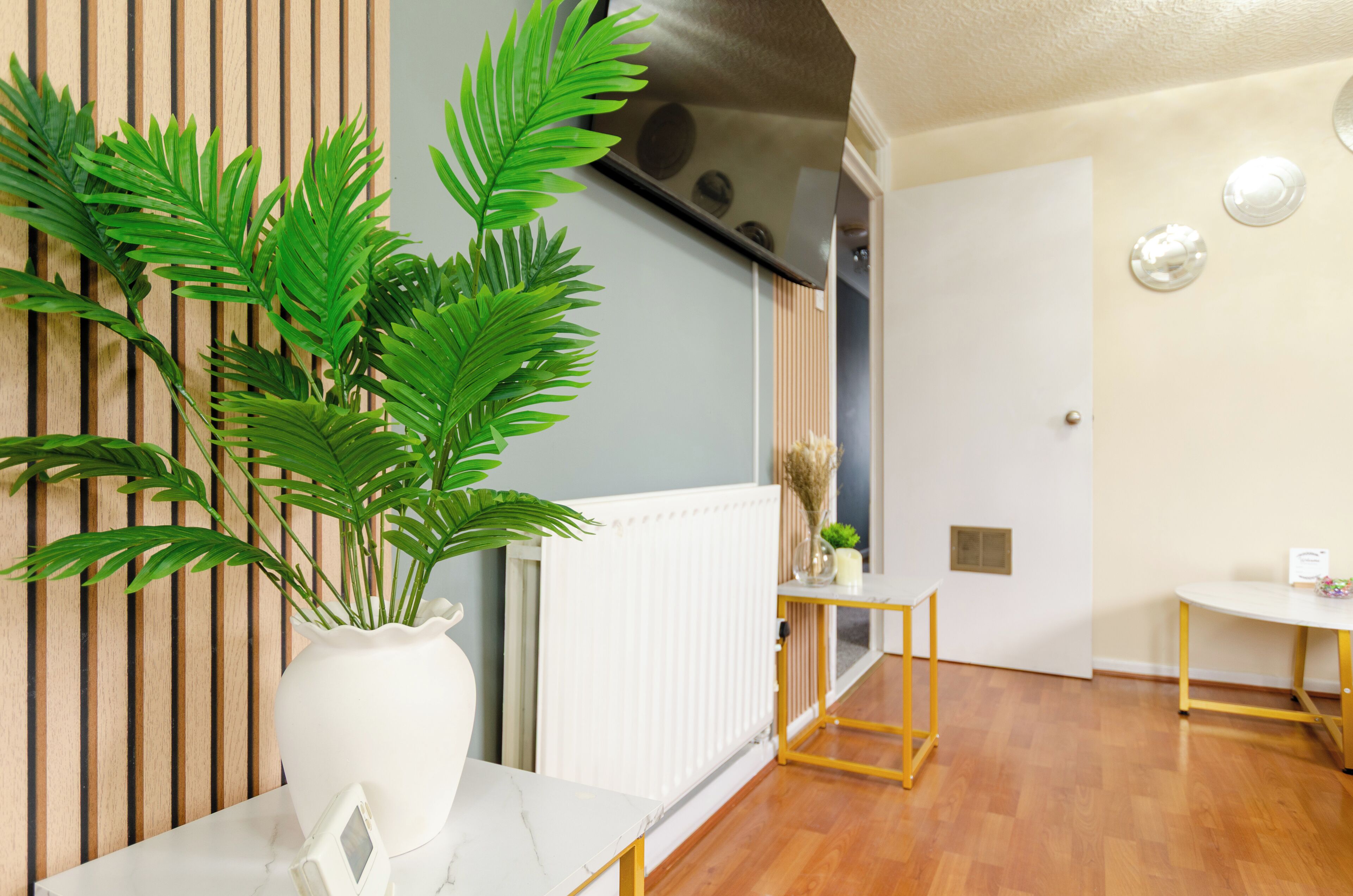 A modern living room with a white marble table, a potted plant, a radiator, and a wooden floor.
