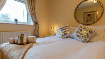 A neatly made bed with patterned pillows, a round mirror on the wall, and a window with curtains.