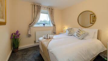 A hotel room with a bed, a window with curtains, a radiator, a wall-mounted mirror, and a potted plant.