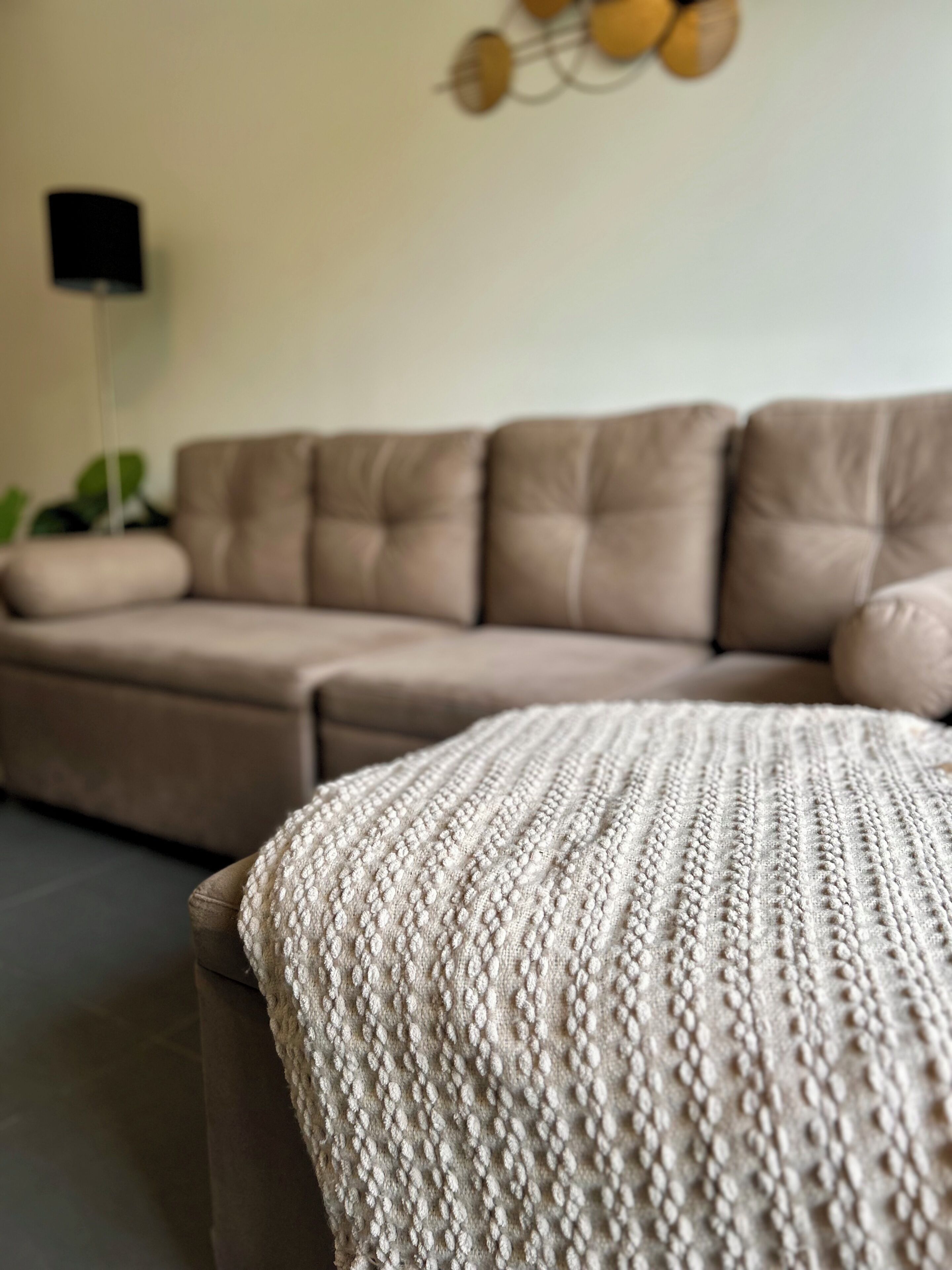 Un canapé beige surmonté d’un plaid à texture dans un salon.