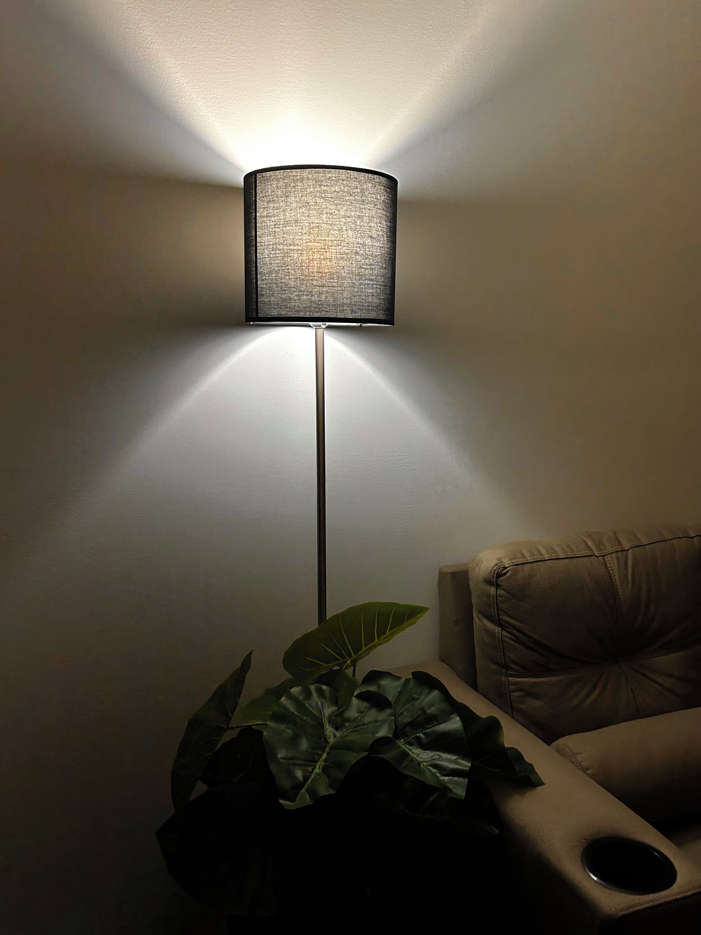 Una lámpara de pie con pantalla texturizada, una planta en maceta y un sofá de cuero en una habitación.