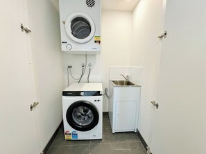 A compact laundry room with a front-loading washer and dryer, a small sink, and a wall-mounted dryer. - Modern 2Brs@ close2 Olympic park (Wentworth Point)