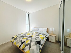 A bedroom with a bed, bedside tables, and a mirror. - Modern 2Brs@ close2 Olympic park (Wentworth Point)