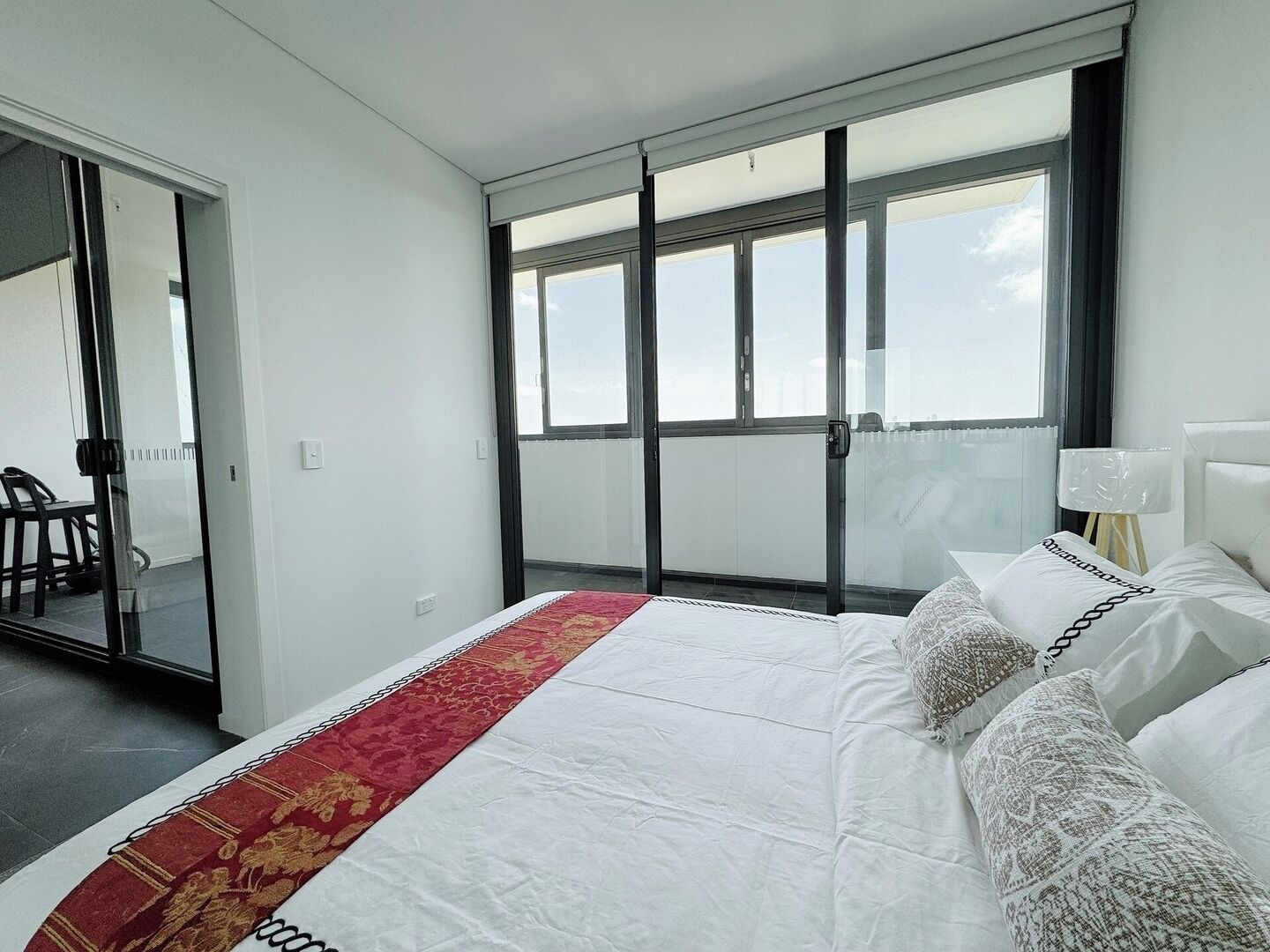 Una camera d'albergo con un letto, un comodino, una lampada e vista attraverso una porta scorrevole.