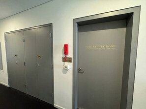 Ein Flur mit zwei grauen Türen, eine als Brandschutztür gekennzeichnet, mit einem roten Notruftelefon und einem Schild, das die Austiegsstufe 7 angibt.