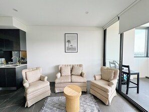 Ein modernes Wohnzimmer mit drei beigen Sesseln, einem runden Holztisch und einem gerahmten Bild an der Wand.