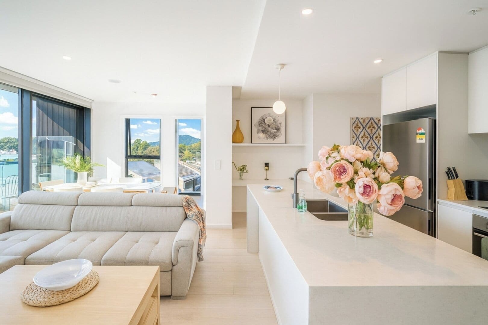 Un salon moderne comprenant un canapé, une table à manger et un coin cuisine avec un réfrigérateur et un vase de fleurs.