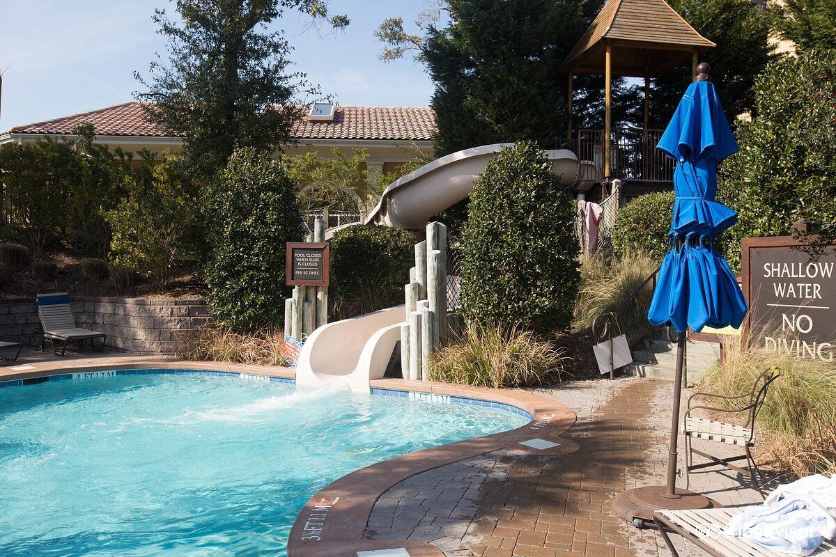 A swimming pool with a slide, a shallow water sign, and a gazebo in the background.