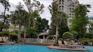Uma piscina com posto de salva-vidas, palmeiras e um edifício ao fundo.