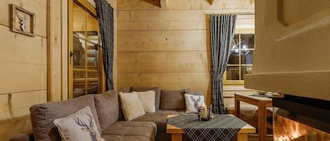 A cozy cabin interior with a wooden interior, a sofa set, a table, and a fireplace.