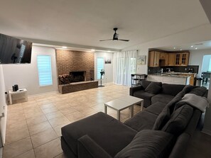Ein modernes Wohnzimmer mit Kamin, einer Couch, einem Couchtisch und einer Küchenzeile im Hintergrund.