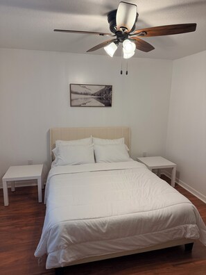 A bedroom with a bed, two bedside tables, a ceiling fan, and a wall-mounted picture. - Capo's Cast Aways Lake House (Haines City)