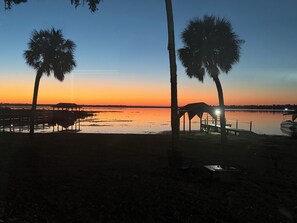 Vista del atardecer con palmeras y un muelle sobre aguas tranquilas.
