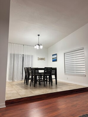A dining area with a table and chairs, a chandelier, a sign that says 'LAKE', and a window with blinds. - Capo's Cast Aways Lake House (Haines City)