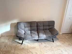 Ein graues Ledersofa mit einer gesteppten Verzierung, auf einem Fliesenboden vor einer schlichten Wand platziert.
