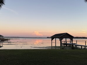 A tranquil lakeside scene with a wooden gazebo and a dock extending into the water. - Capo's Cast Aways Lake House (Haines City)