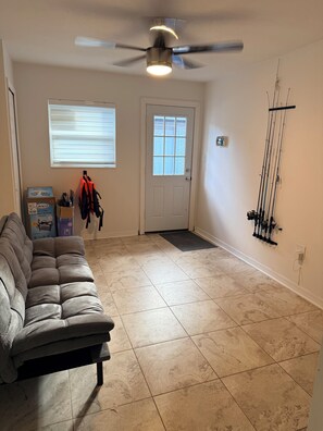 Ein Zimmer mit Deckenventilator, einer Tür mit Fenster, einem grauen Sofa und an der Wand befestigten Angelruten.