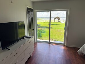 Ein Zimmer mit Fernseher auf einer Kommode, eine Glastür zur Terrasse mit Blick auf das Wasser.