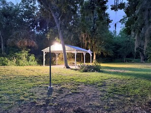 A gazebo with a roof and walls, surrounded by grass and trees. - Capo's Cast Aways Lake House (Haines City)