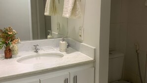 Ein Badezimmer mit Waschbecken, Spiegel und Schränken. Ein WC und eine Duschkabine sind ebenfalls zu sehen.