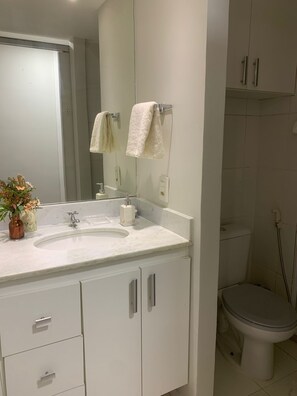 A bathroom with a white sink, mirror, and cabinets. There is a toilet and a shower area visible. - Olympic Bar well located (Rio de Janeiro)