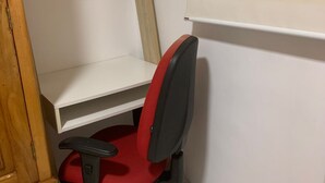 Ein Arbeitsplatz in der Ecke mit einem roten Bürostuhl, weißen Regalen und einem Holzschrank.