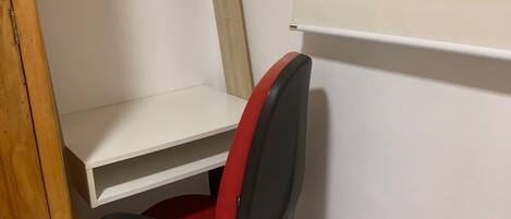 A corner workspace with a red office chair, white shelving, and a wooden cabinet.
