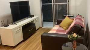 Ein modernes Wohnzimmer mit Flachbildfernseher, Schreibtisch, Sofa und einem kleinen Tisch mit einer Vase.