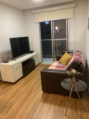A modern living room with a flat-screen TV, a desk, a sofa, and a small table with a vase. - Olympic Bar well located (Rio de Janeiro)