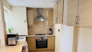 A modern kitchen with wooden cabinets, a built-in oven, a gas stove, and a coffee maker.