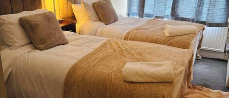 A hotel room with two beds, a nightstand, a lamp, and a chair.