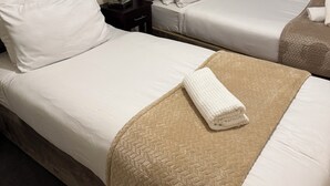 A hotel room with two beds, each with white bedding and a brown quilt. There is a nightstand with a lamp between the beds.