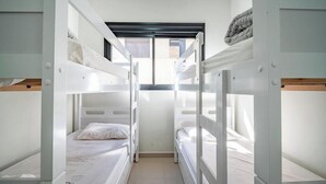 Habitación con literas, tragaluz, ropa de cama blanca y vistas al exterior.