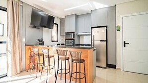 Una cocina moderna con una isla central, taburetes de bar, un televisor de pantalla plana y electrodomésticos integrados.
