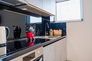Una cocina moderna con encimera negra, electrodomésticos de acero inoxidable y una ventana que deja entrar luz natural.