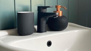 A white bathroom sink with a black faucet and a black soap dispenser. - Blues Point Hotel (McMahons Point)