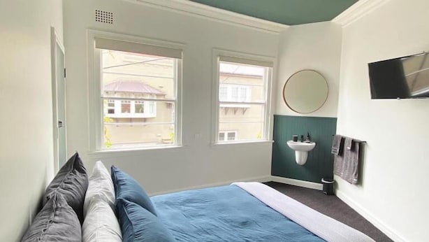 A bedroom with a bed, pillows, a window, a sink, and a television. - Blues Point Hotel (McMahons Point)