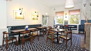 A dining area with a patterned floor, wooden tables and chairs, a bench, and wall-mounted lighting. - Blues Point Hotel (McMahons Point)