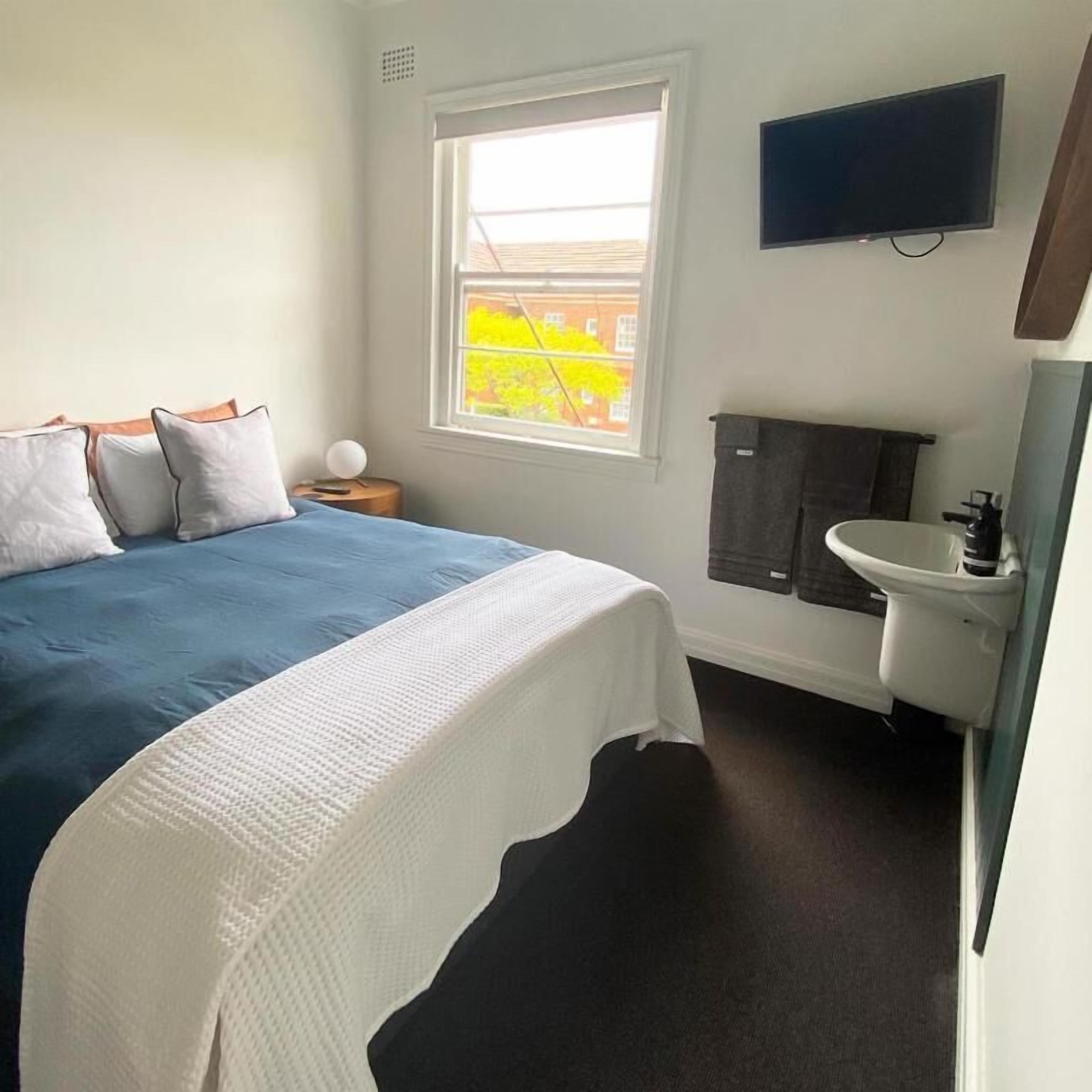 A bedroom with a bed, a window, a television, a sink, and a mirror.