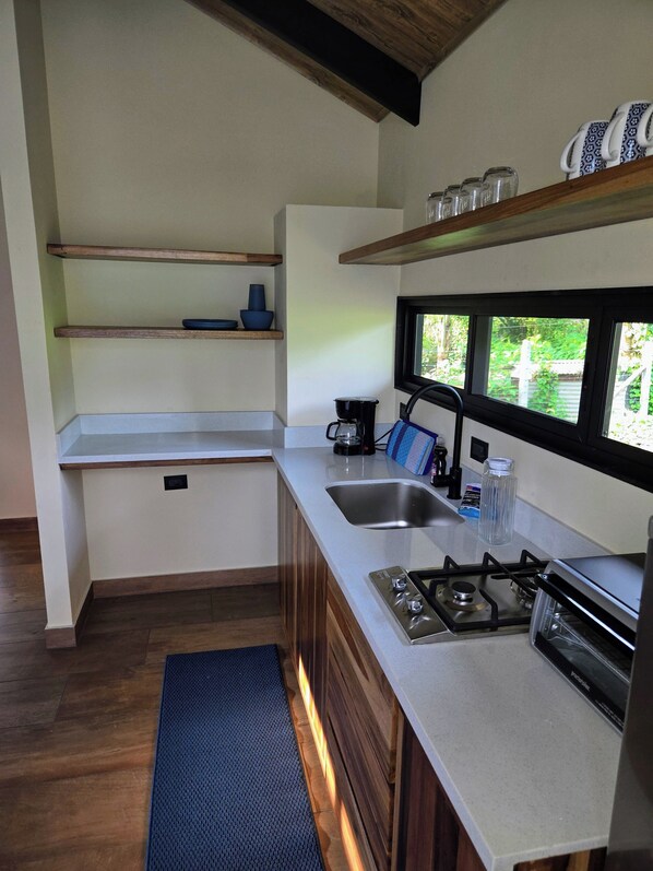 A modern kitchen with wooden cabinets, a built-in gas stove, a stainless steel sink, and a window providing a view of greenery outside.